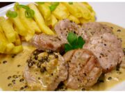 Luxuriöses Schweinefilet mit grüner Pfeffersauce und Cognac Schweinefilet flambiert mit Cognac in der Pfanne – intensive blaue und orange Flammen über grünem Pfeffer