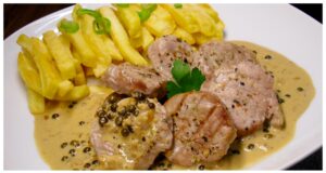Luxuriöses Schweinefilet mit grüner Pfeffersauce und Cognac Schweinefilet flambiert mit Cognac in der Pfanne – intensive blaue und orange Flammen über grünem Pfeffer