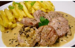 Luxuriöses Schweinefilet mit grüner Pfeffersauce und Cognac Schweinefilet flambiert mit Cognac in der Pfanne – intensive blaue und orange Flammen über grünem Pfeffer