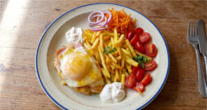 Hähnchenbrust mit Schinken, Käse und Pfirsich: Retro-Mittagessen mit Pommes Hähnchenbrust mit Schinken, Käse und Pfirsich auf einem Teller mit Pommes