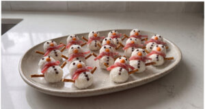 Raffaello-Kugeln als Schneemänner: Ungebackene Weihnachtsplätzchen mit einfacher Dekoration Raffaello-Schneemänner auf einem Teller dekoriert