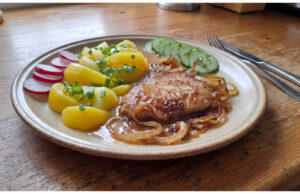 Schweineschnitzel mit Zwiebelsoße: Saftiges Fleisch dank langer Marinade Schweineschnitzel mit Zwiebelsoße und Kartoffeln auf einem Teller