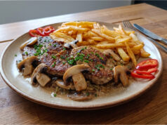 Schweineschulter mit Champignons: Saftiges Fleisch mit cremiger Sauce und hausgemachten Pommes Schweineschulter mit Champignons und hausgemachten Pommes auf einem Teller
