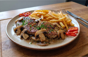 Schweineschulter mit Champignons: Saftiges Fleisch mit cremiger Sauce und hausgemachten Pommes Schweineschulter mit Champignons und hausgemachten Pommes auf einem Teller