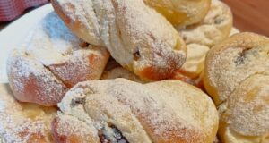 Hefeschnecken mit Quark und Rumrosinen: Luftiges Gebäck zum Kaffee Mit Puderzucker bestäubte Hefeschnecken auf einem Teller.