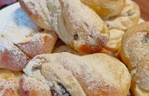 Hefeschnecken mit Quark und Rumrosinen: Luftiges Gebäck zum Kaffee Mit Puderzucker bestäubte Hefeschnecken auf einem Teller.