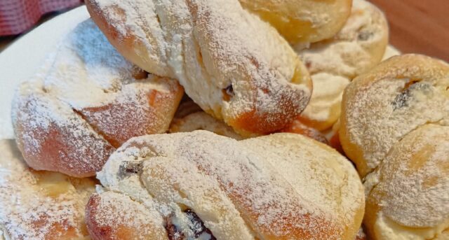 Hefeschnecken-mit-quark-und-rumrosinen Mit Puderzucker bestäubte Hefeschnecken auf einem Teller.