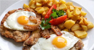Holsteiner Schweineschnitzel: Saftiges Fleisch mit Spiegelei, Speck und knusprigen Kartoffeln Holsteiner Schweineschnitzel mit Spiegelei und Speck auf Kartoffeln serviert