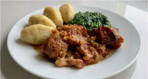 Schweinebraten mit Kartoffelklößchen und Spinat: Langsam geschmortes Mittagessen mit Biersoße Schweinebraten mit Kartoffelklößchen und Spinat auf einem Teller serviert