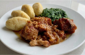 Schweinebraten mit Kartoffelklößchen und Spinat: Langsam geschmortes Mittagessen mit Biersoße Schweinebraten mit Kartoffelklößchen und Spinat auf einem Teller serviert